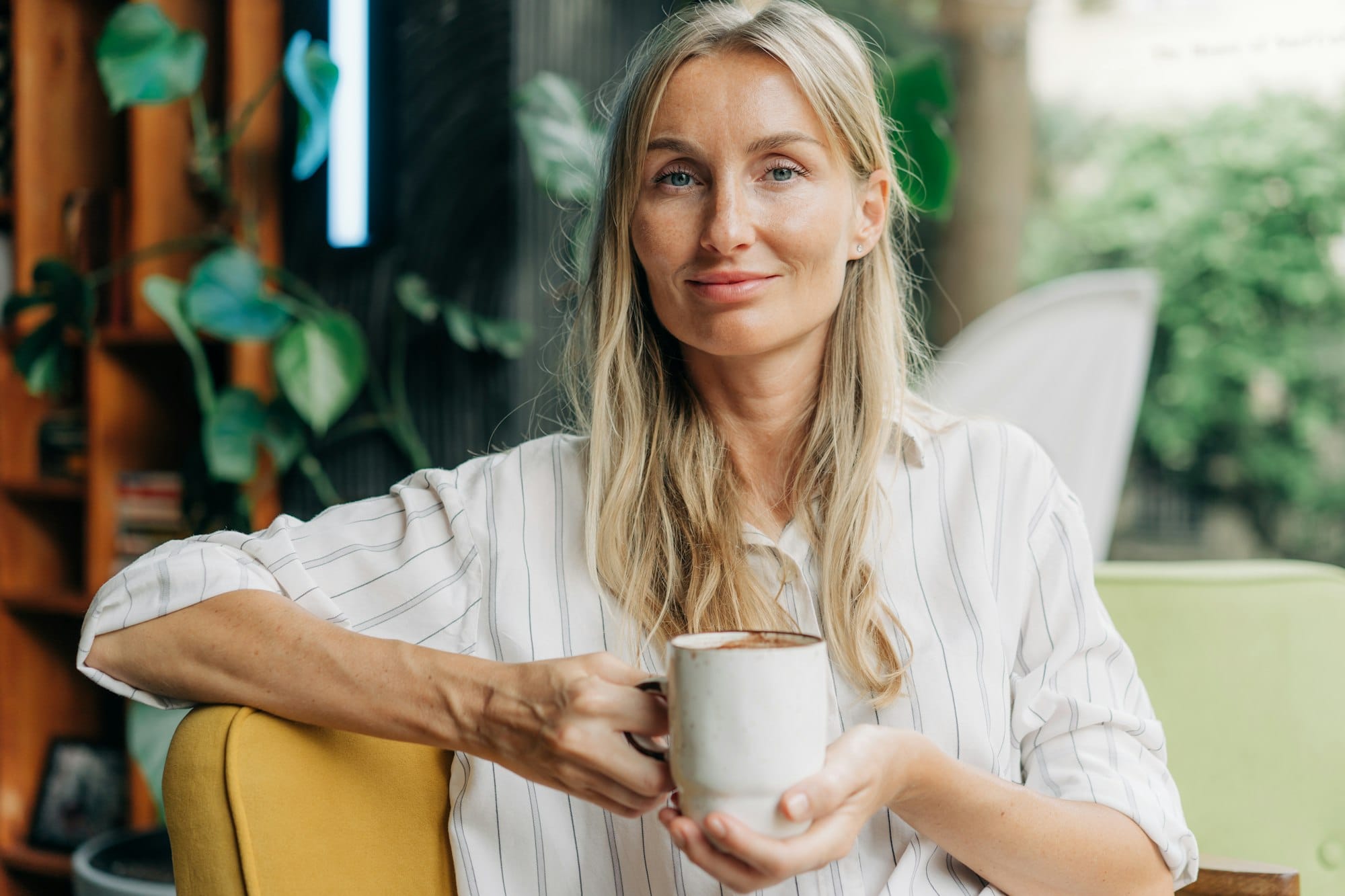 Testimonial portrait of a young woman with a mug of coffee sitting in a modern coffee shop.